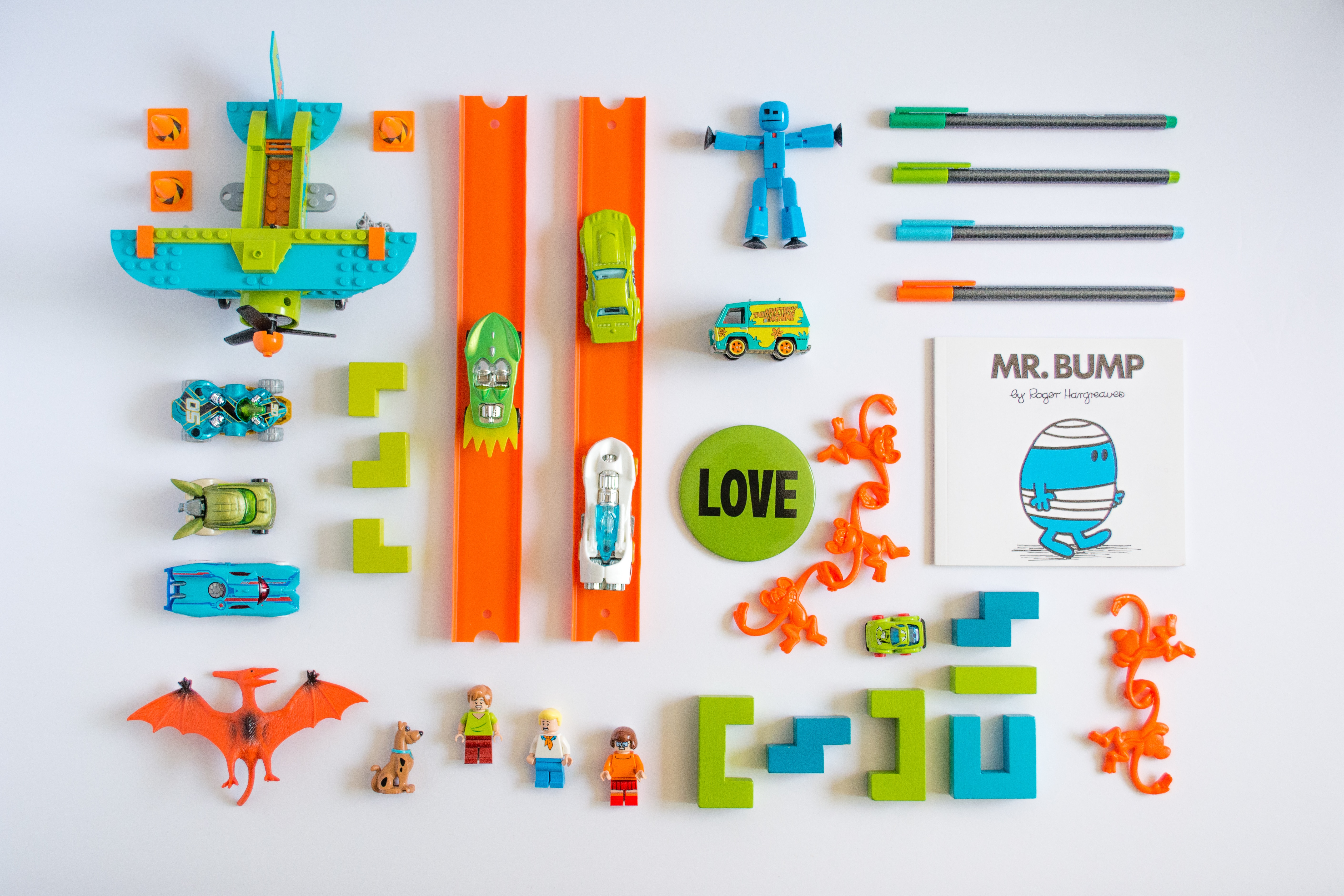 Orange toys neatly organized in a rectangular area, comprised of lego, dinosaurs, race cars, books, robots, monkeys, and a button that says love.