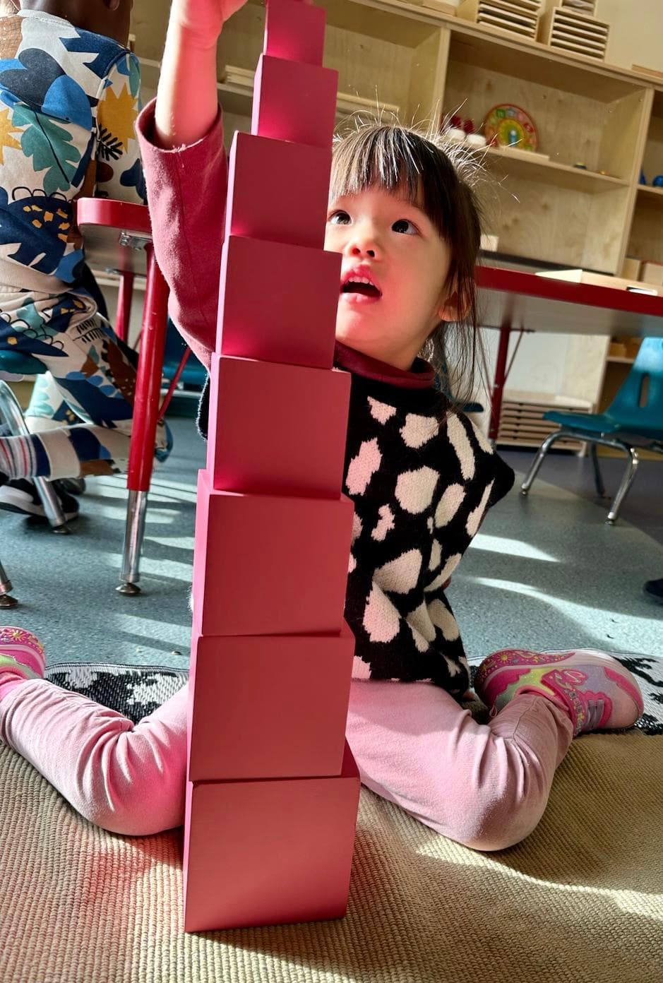 A girl excitedly creating a tall structure of stacked red cylinders.
